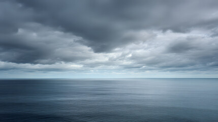 Fototapeta premium Dramatic dark storm clouds over a calm deep blue ocean horizon, creating a moody and atmospheric seascape background.