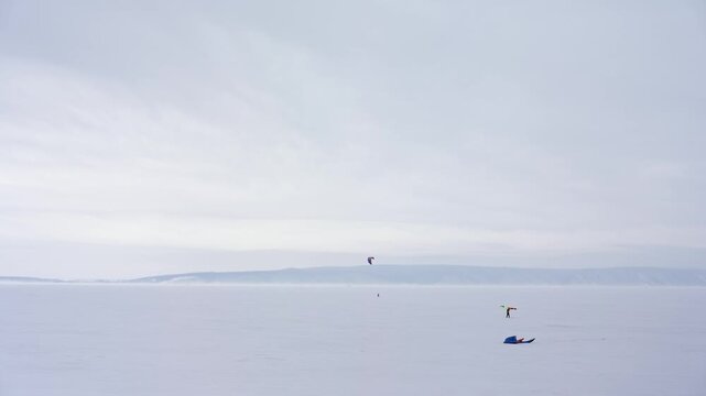 A daring snowkiter carves paths across a vast, flat, frozen lake under an ethereal overcast sky.