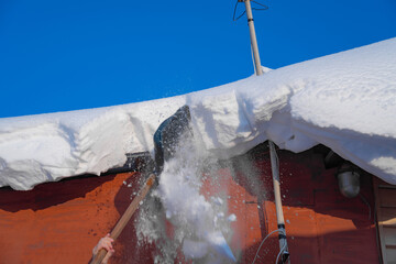 snow drifts on the roof of the house, dangerously overhanging boulders, snow removal with a shovel