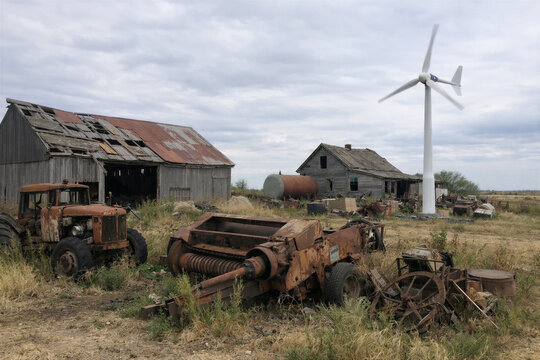 Abandoned farmstead with wind turbine and rusted machinery