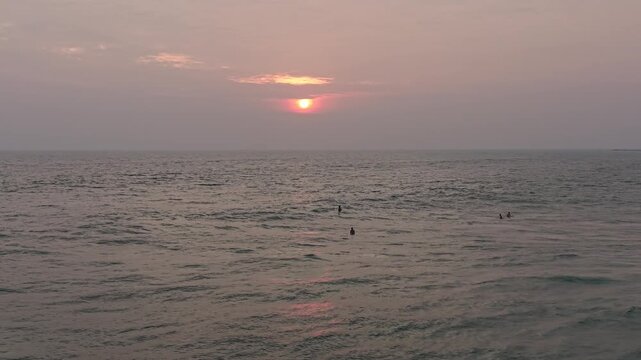 Silhouetted surfers waiting for waves at sunset on a tropical beach in Sri Lanka. Warm sunlight reflecting on the ocean surface, serene evening mood, and exotic coastal scenery. Concept of travel dest