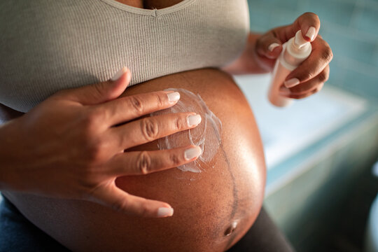 Pregnant woman applying lotion on belly at home