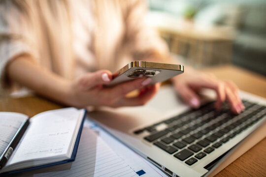 Person multitasking on smartphone and laptop at home office desk