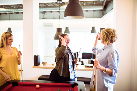 Three coworkers playing pool and high-fiving in modern office