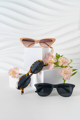 Obraz premium Trendy sunglasses in plastic frames on white background with flowers. Sunglasses special offer, summer sale, discount. Optic shop promotion banner. Eyewear fashion. vertical, copy space, minimalism