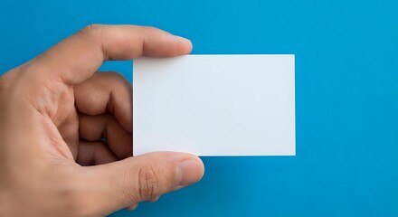 Obraz premium Hand holding blank white business card on blue background for mockup design and branding presentation.