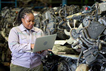 Technician working with a laptop in a scrap yard, assessing the metal pile