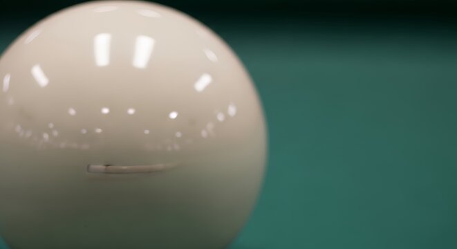Close-up of a pristine white cue ball resting on a vibrant green billiard table, ready for a game of pool.