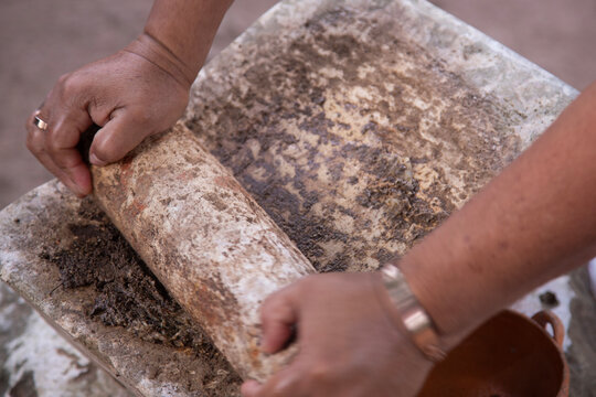 Preparing Mexican black recado on a traditional metate in the Yucatan Peninsula. A paste of spices and chilies used in Yucatecan cuisine.
