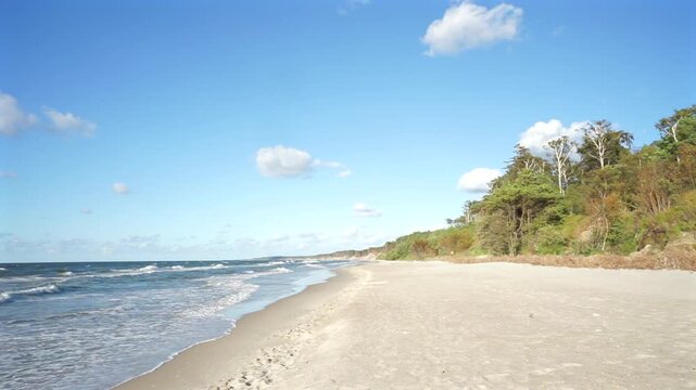 Baltic Sea sandy beach with gentle waves and blue sky on a sunny summer day, calm empty coastline landscape in July