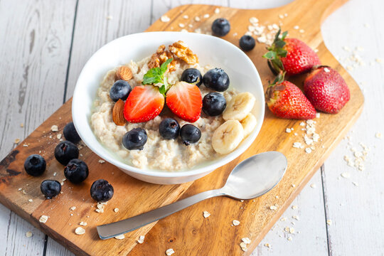 creamy oats porridge topped with strawberries, bananas, blueberries, nuts, and mint beside spoon