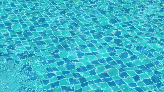 Water surface with tiles inside pool. The sun reflects light, creating playful patterns and a refreshing feel. The tile pattern shows, forming a grid of shapes
