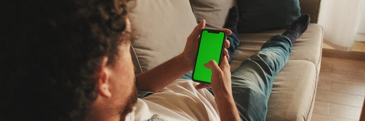 Guy dressed in denim shirt has lunch, sits in the living room and emotionally watches sports game on TV. Panoramic © Andrii Nekrasov