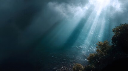 Naklejka premium Atmospheric sunbeams break through dark clouds illuminating the rippling surface of a moody sea with foliage on the shore