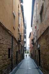 Obraz premium Persona caminando por una calle estrecha y antigua con fachadas de piedra y colores cálidos en Logroño, España
