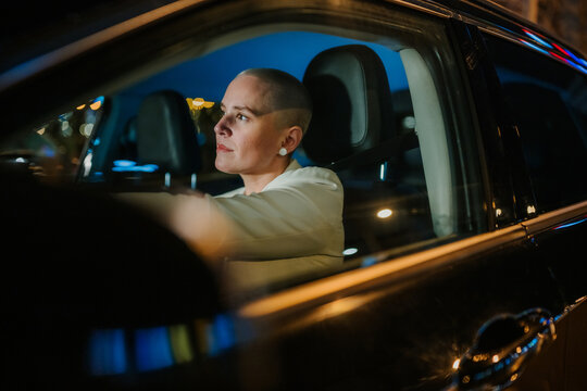 Woman with buzz cut hair driving a car in the city at night, reflecting independence and urban life