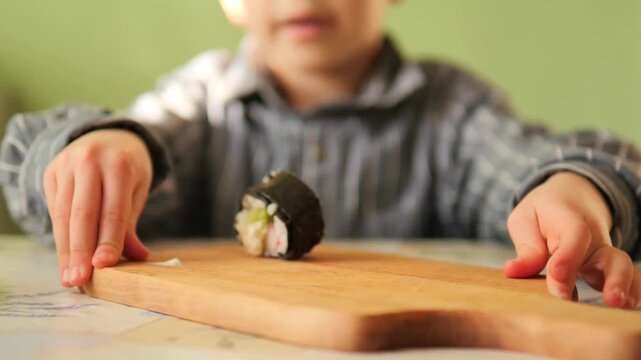 close-up of a child's hands resting near a fresh maki sushi roll on a wooden board - Nutritious homemade Japanese cuisine for kids in smooth slow-mo, featuring fresh ingredients