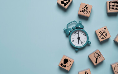 Alarm clock with business strategy icons on wooden blocks representing time management, goal setting and productivity planning. Corporate scheduling and performance growth concept with copy space.