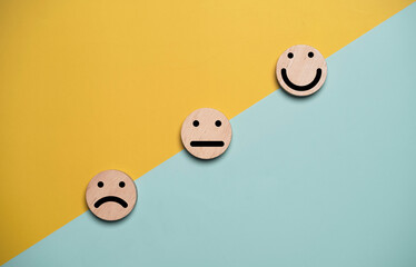 Customer satisfaction concept with wooden emotion icons from sad to happy on colorful background. Service quality improvement, feedback rating and experience evaluation theme with copy space.
