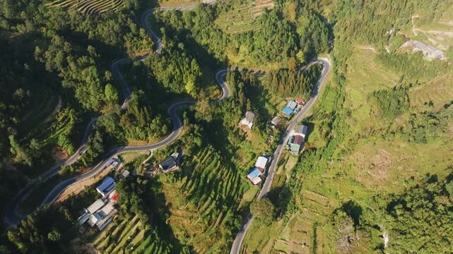 A winding road snakes through the lush, green mountains of Dong Van, Ha Giang, Vietnam. Terraced fields and small villages dot the landscape, showcasing rural life.