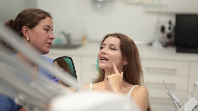 Joyful young woman in dentist office looking at her healthy teeth in the mirror. Woman dentist shows a client clean teeth. High quality 4k footage