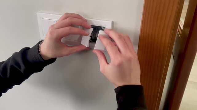Hands installing white decorative frame and buttons on a triple light switch, final stage of electrical work.