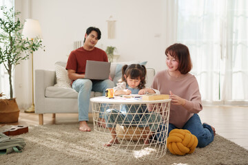 Asian family drawing together at home with father watching daughter and mother