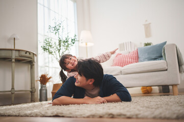 Asian father giving piggyback ride to daughter while playing at home