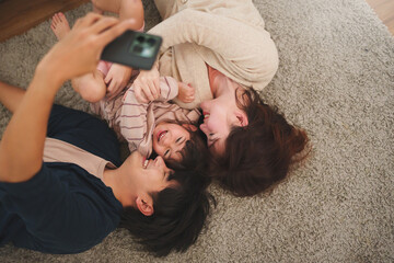Asian family taking selfie with smartphone together lying on carpet at home