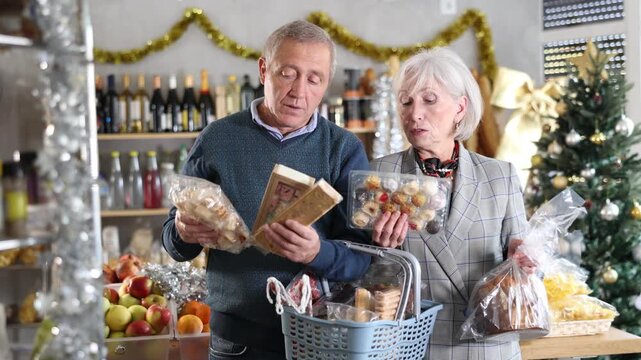 Elderly spouses looking at sweets in store. Market visitors choose consider nougat, panettone, marzipan, cookies, chocolate. Customers choose national European sweet desserts in sales area