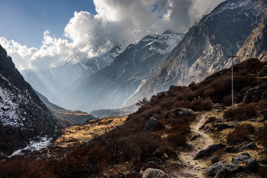 Dramatic light filtering through clouds and peaks over narrow Langtang Valley trail flanked by steep mountains near Kyanjin Gompa