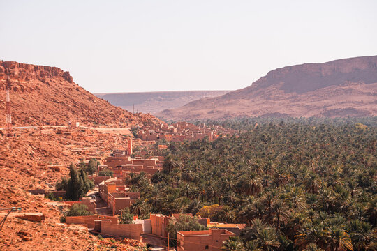 Aerial view of palm-filled oasis and red clay village nestled between rugged desert cliffs in the Ziz Valley, near Errachidia, Morocco