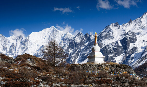 White Buddhist stupa in Langtang Valley, Nepal, with dramatic backdrop of snow-covered Gangchempo, and surrounding Himalayan peaks under a clear blue sky