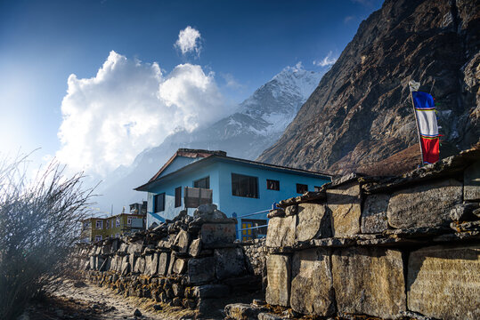 Blue teahouse and prayer flags under dramatic clouds along the trekking route in Langtang Valley, Nepal