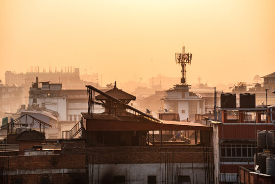 Urban rooftop silhouette of Kathmandu at sunset with dramatic haze and communication towers rising in the skyline