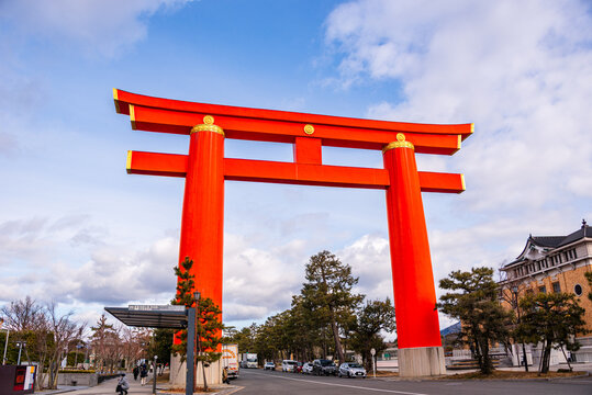 Urban street scene in Kyoto with a bright red torii gate spanning the road, surrounded by buildings and leafless winter trees