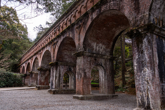 Historic red brick arches of the Suirokaku Aqueduct nestled among tall cedar trees in the temple grounds of Nanzen-ji, Kyoto