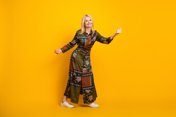 Obraz premium Elegant mature woman wearing a patchwork dress smiles and poses against a vibrant yellow background for a stylish casual fashion image