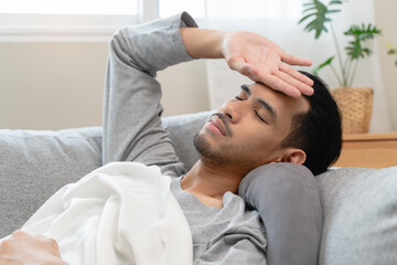 Obraz premium Seasonal cold sickness in people concept, Sick asian man looking at thermometer during measuring his body temperature feel exhausted and headache from fever.