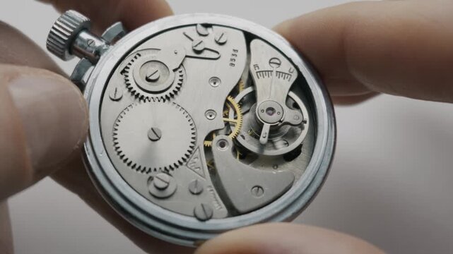 Hands hold an open silver pocket watch revealing the internal gear mechanism and oscillating balance wheel. This shot highlights precision engineering and the passage of time.