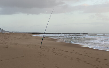 fishing rods stand on a sandy beach, silhouetted against a breathtaking and colorful sunrise over the tranquil ocean.