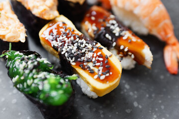 A colorful selection of sushi on a black plate with various toppings