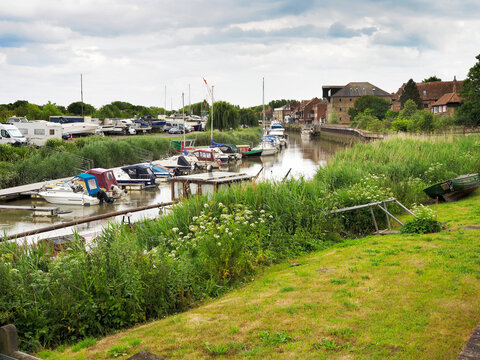 View of River Stour lined with boats at Sandwich Kent bordered by green grass and buildings in the background