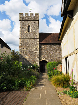 Visitors walk along stone path leading to St Paters Church, framed by flowering plants, in Canterbury Kent during a sunny day