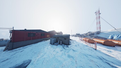 A small group of red and gray buildings stands on a snowy hill under a radiant sun. Communication towers rise above the snowy landscape, creating a stark contrast with the bright blue sky. © icetray
