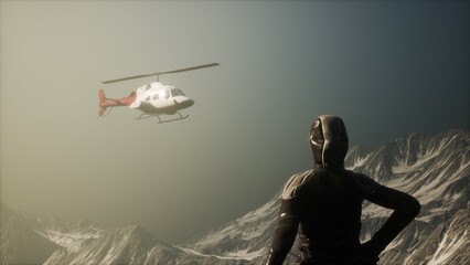 A figure stands resolutely on a rocky outcrop, overlooking majestic snow covered mountains as a helicopter buzzes above, enhancing the sense of adventure in the hushed landscape. © icetray