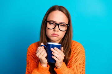 Young woman in orange sweater holding blue mug smiles at camera against blue background