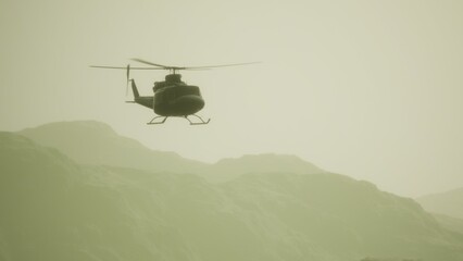 Fototapeta premium A helicopter glides smoothly through a hazy sky, its silhouette framed by distant mountains. The golden light of sunset bathes the landscape, creating a peaceful scene.