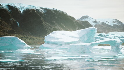 Icebergs drift gracefully in crystal clear waters, reflecting the sunlight. Towering mountains frame the scene, creating a tranquil atmosphere in this remote arctic paradise. © icetray