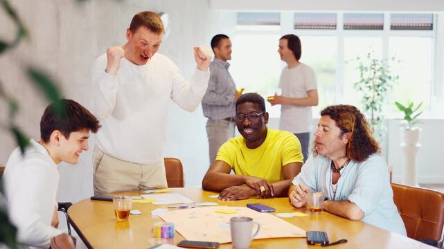 Positive adult man playing board game with interest with male friends of different nationalities during bachelor party